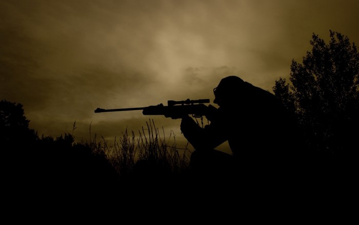 Silhouette of a sniper aiming a rifle at dusk