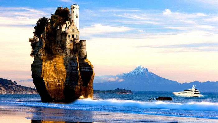 Castle on a rock formation with a yacht and snowy mountain