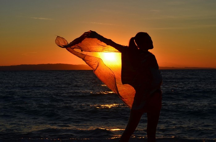Silhouette of a woman with a scarf at sunset over the sea