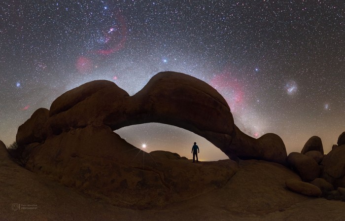 Silhouette under rock arch with starry sky