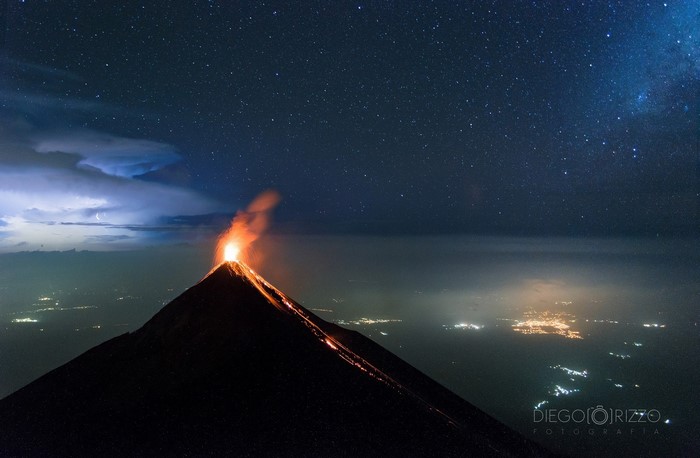 Volcano erupting at night under a starry sky with lightning