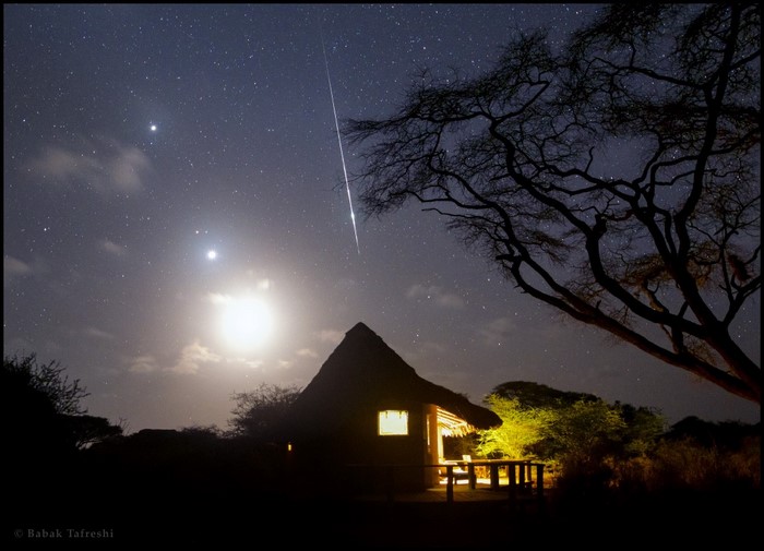 Meteor shower over a thatched hut at night