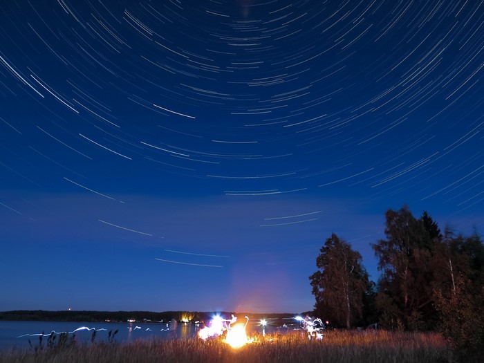 Star trails over a lake with a campfire at night