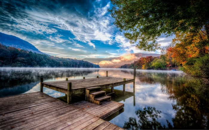 Wooden pier on a misty lake with autumn trees and mountains