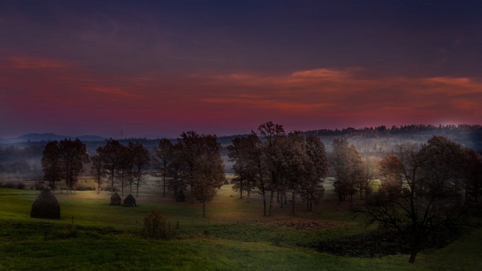 Sunset over a misty landscape with trees and haystacks