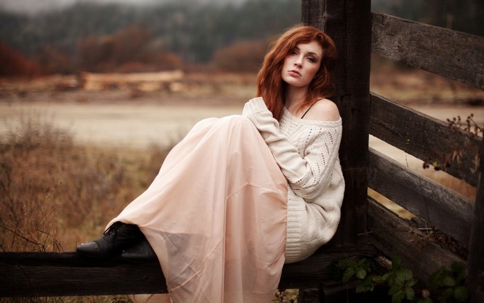 Redhead woman in sweater and skirt sitting on fence