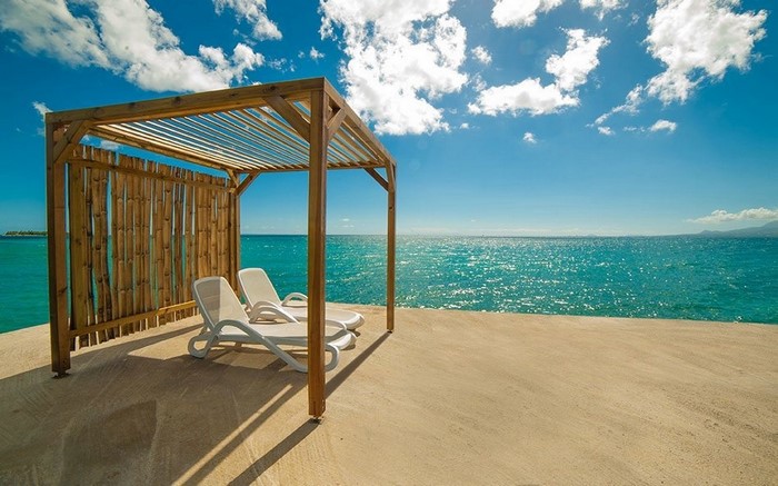 Beach lounge chairs under a wooden sunshade by the ocean