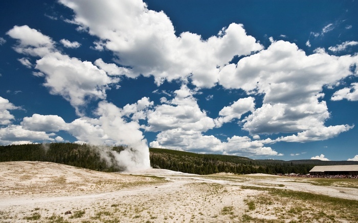 Old Faithful Geyser erupting under a cloudy blue sky