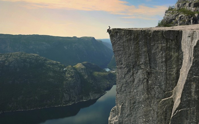 Person sitting on the edge of a cliff overlooking a fjord in Norway