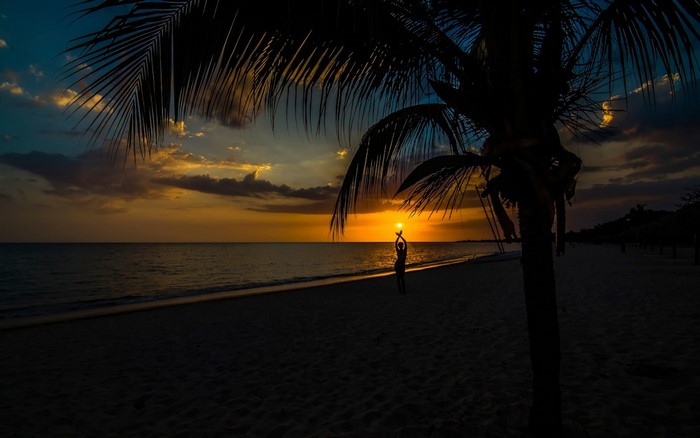 Silhouette of a person holding the sun on a beach at sunset