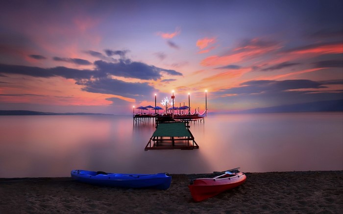 Kayaks on beach at sunset with pier in water