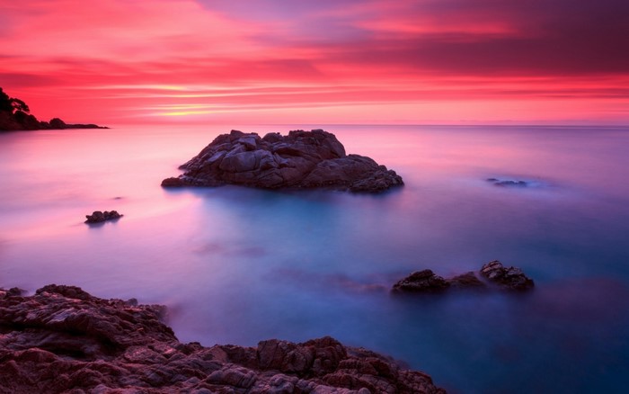 Sunset over the ocean with rocks and colorful sky