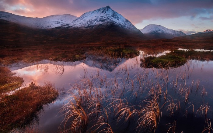 Snow-capped mountains reflected in a misty loch at sunrise