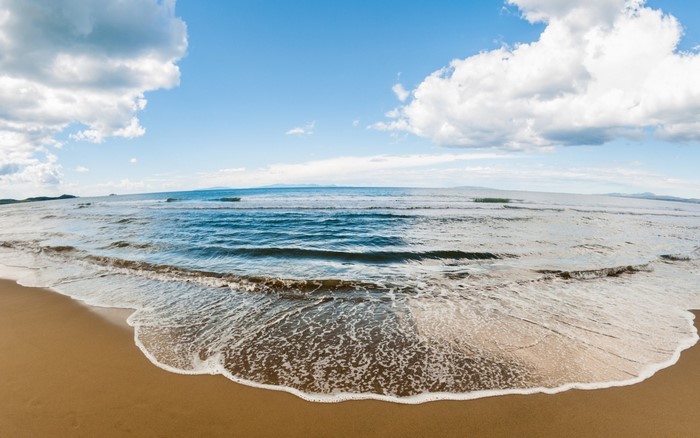 Sandy beach with waves under a cloudy blue sky