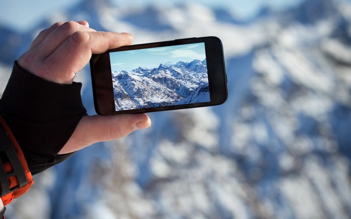 Hand holding smartphone showing snowy mountains