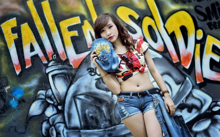 Woman in jean shorts holding a studded bag in front of graffiti
