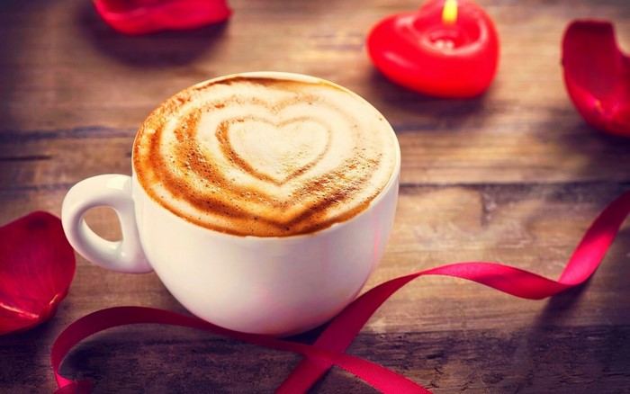 Cappuccino with heart art, rose petals, and heart candle