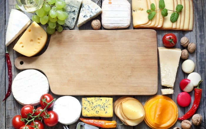 Assortment of cheeses, grapes, tomatoes, and peppers on a wooden surface