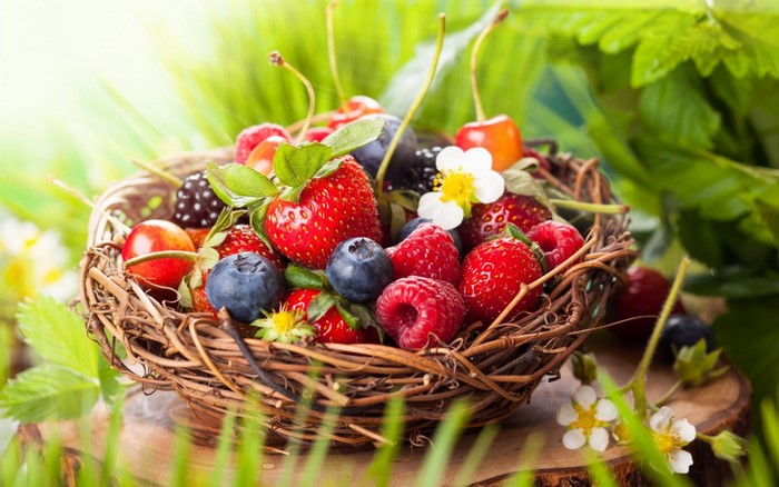 Basket of fresh berries and flowers on a wooden surface