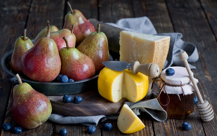 Pears, cheese, blueberries, and honey on a wooden surface