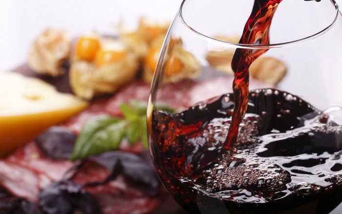 Red wine being poured into a glass with a charcuterie board