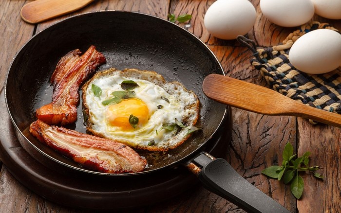 Fried egg and bacon in a pan with whole eggs