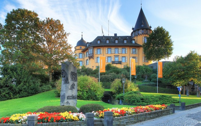 Yellow castle with a conical tower and flower garden