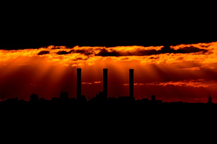 Factory chimneys silhouetted against a dramatic sunset sky