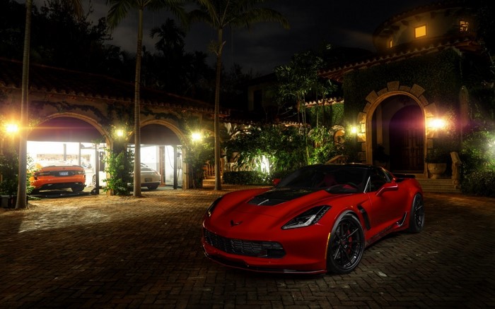Red Chevrolet Corvette parked in front of a mansion at night