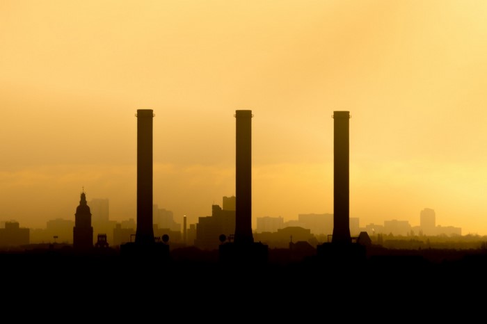 Three smokestacks silhouetted against a hazy sunset sky