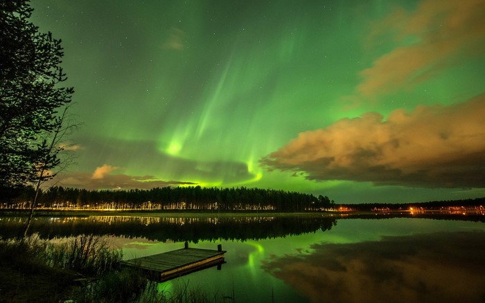 Aurora Borealis over a lake with a forest and dock