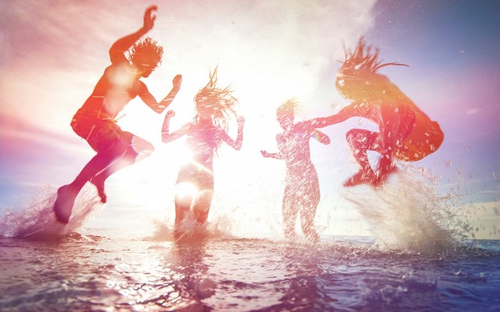 People jumping in the ocean at sunset