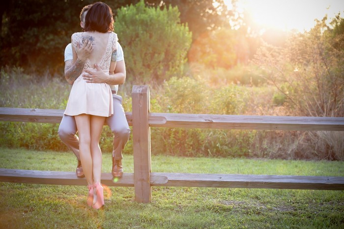 Couple embracing by a wooden fence at sunset