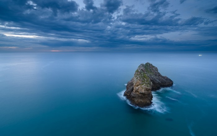 Rock formation in the sea under cloudy sky