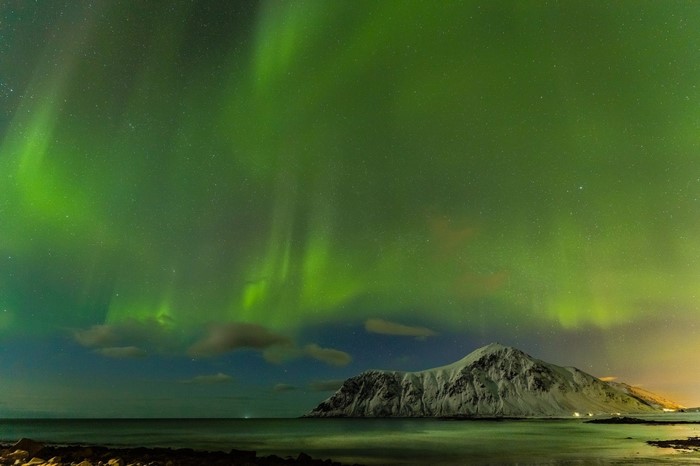 Aurora Borealis over a snowy mountain and ocean