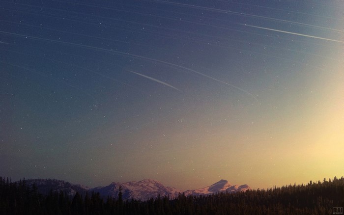 Starry night sky over mountains and forest