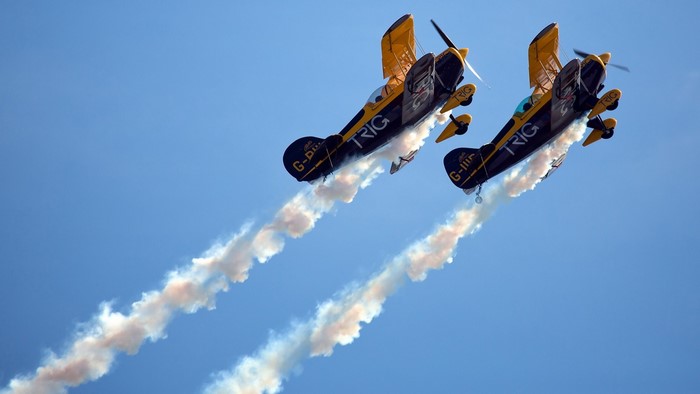 Two biplanes performing aerobatics with smoke trails