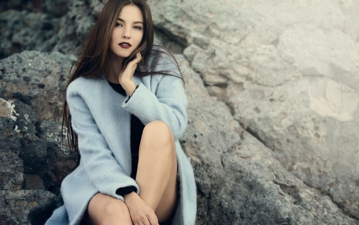 Woman in blue coat sitting on rocks