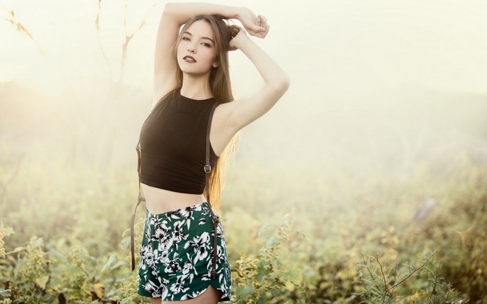 Woman with long brown hair wearing a black top and floral shorts