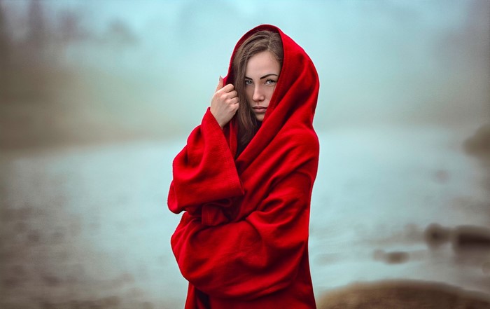 Woman in red hooded robe by a misty body of water