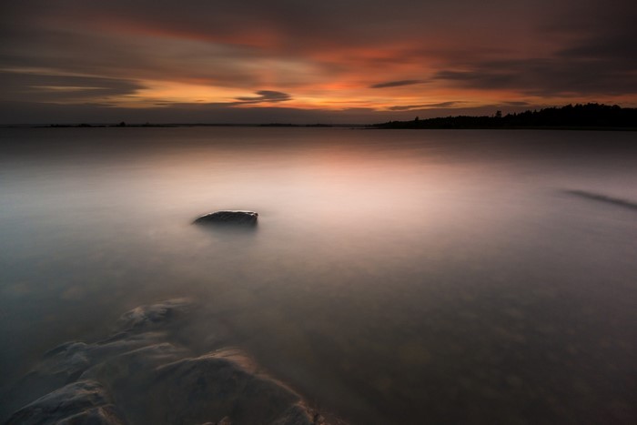 Sunset over a calm body of water with a rock