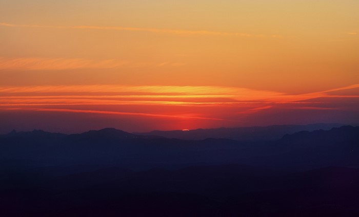 Sunset over silhouetted mountains with orange and red sky