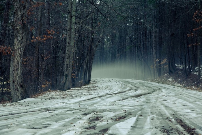 Winding snowy road through a dark, misty forest