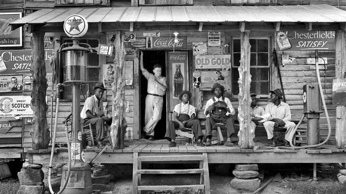 Men gathered at a roadside store with Texaco gas pump