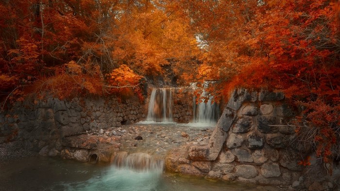 Autumn waterfall with red and orange trees and stone walls