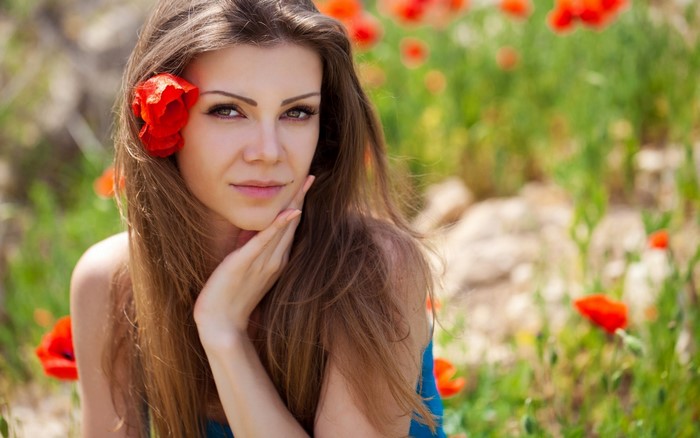 Woman with a red flower in her hair in a poppy field