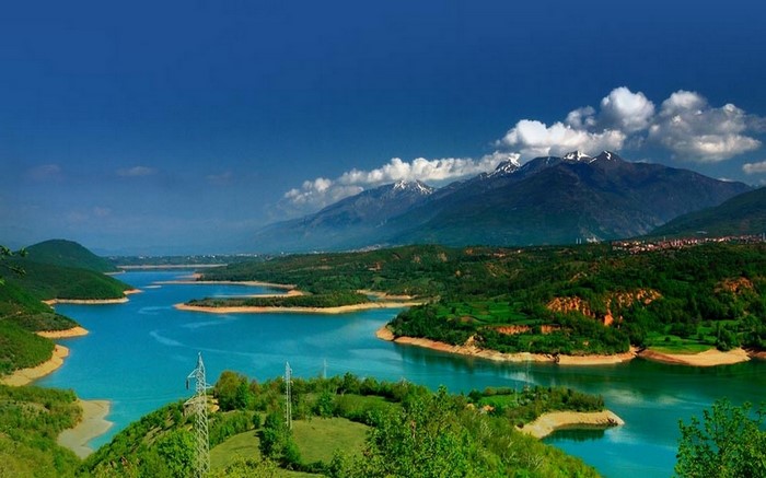Turquoise reservoir surrounded by green hills and snow-capped mountains