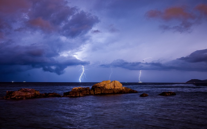 Lightning strikes over the ocean near rocks