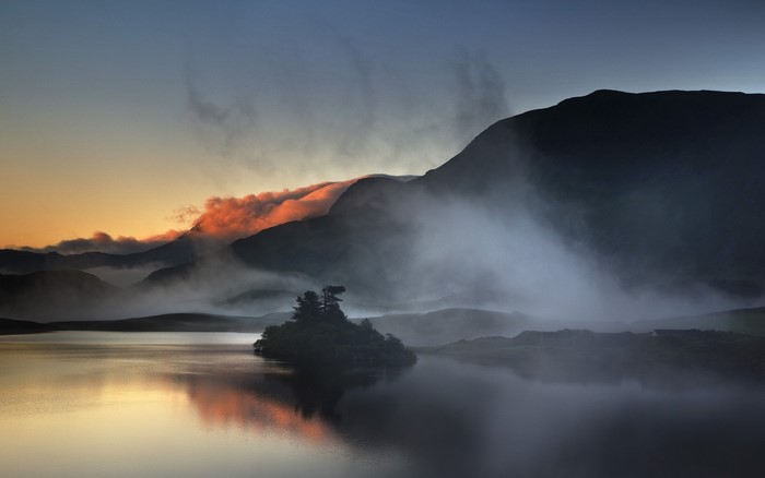 Misty mountains reflected in a calm lake at sunrise