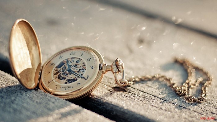 Gold pocket watch with chain on wooden surface